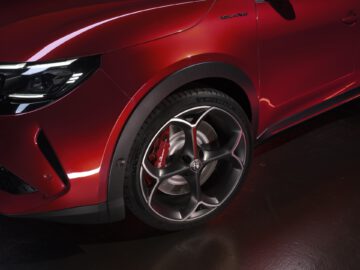 Primer plano de la rueda delantera y el alerón de un coche rojo, destacando el diseño de las llantas de aleación y el emblema 