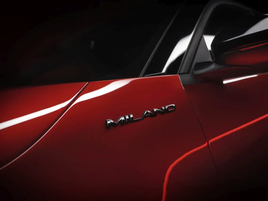 Close-up van het paneel van een rode auto met de naam "Alfa Romeo MILANO" erop gegraveerd.