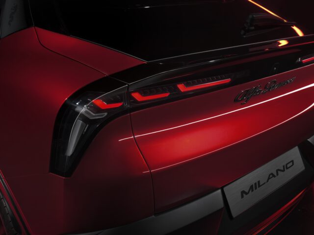 Close-up van het achterlicht en het embleem van een rood voertuig, met de afbeelding "Alfa Romeo MILANO".