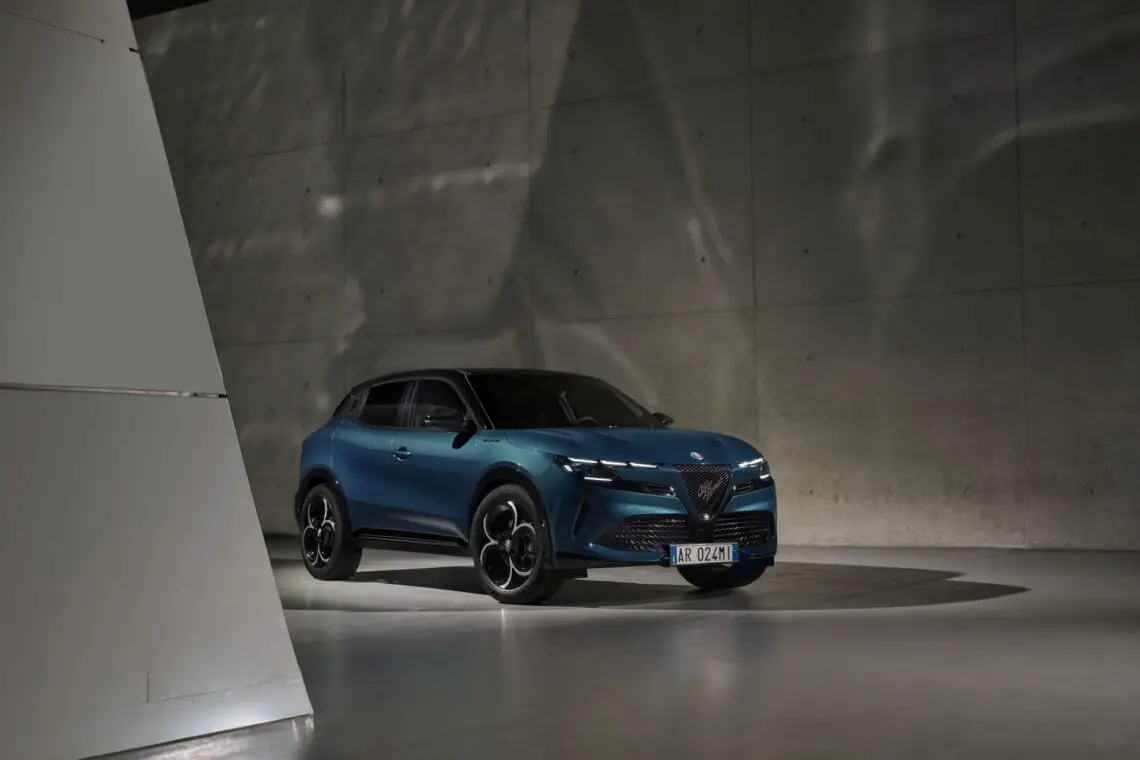 A blue Alfa Romeo parked in a modern concrete structure with dramatic lighting.