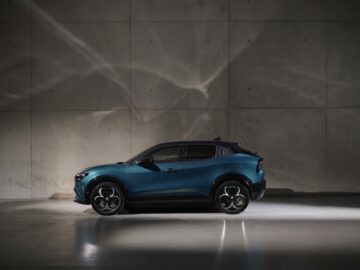 Een blauwe elektrische SUV geparkeerd in een slecht verlichte betonnen ruimte met dramatische verlichting die schaduwen op de muur werpt en het silhouet van een Alfa Romeo MILANO laat zien.