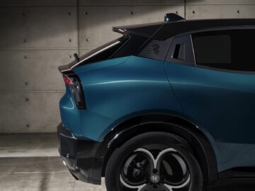 Close-up van het achterpaneel en het wiel van een moderne Alfa Romeo MILANO blauwe SUV tegen een betonnen muurachtergrond.