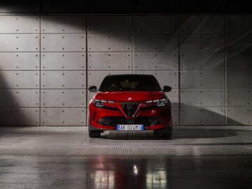 Roter Alfa Romeo geparkt vor einer Betonwand mit dramatischer Beleuchtung.