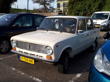 A vintage Lada 1200 parked in a parking lot, with a distinctive grille and rectangular headlights.