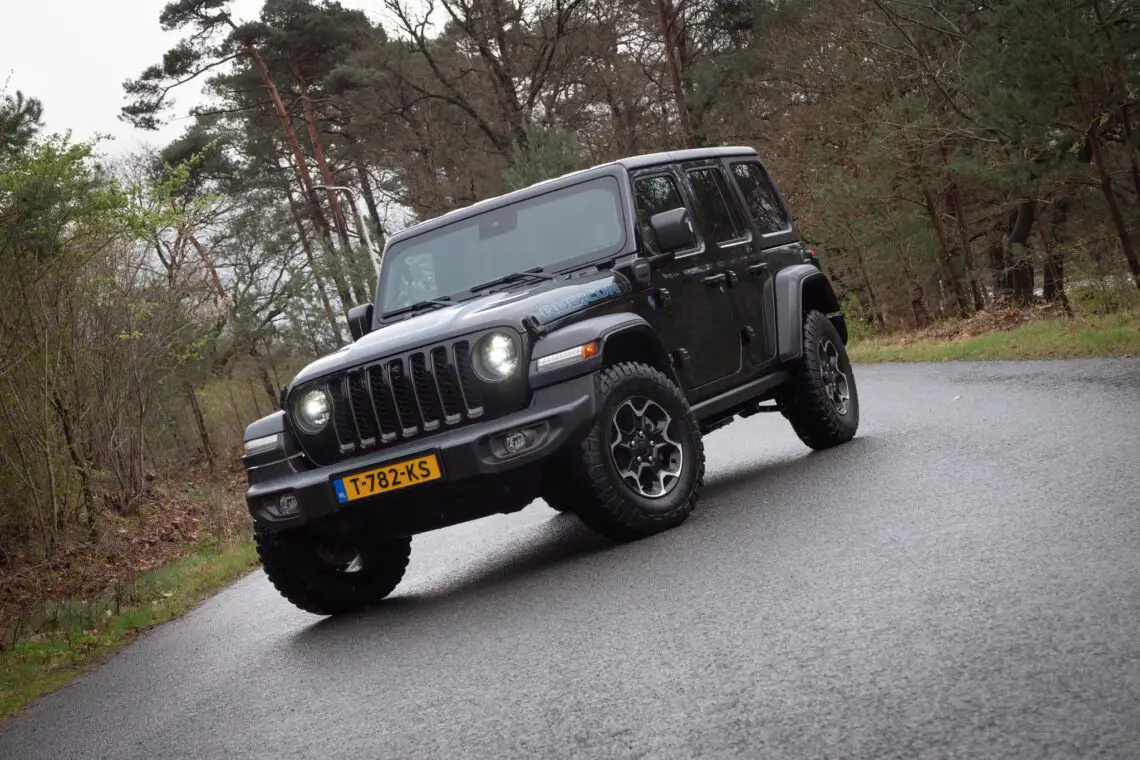 A black Jeep Wrangler 4xe parked on an asphalt road with trees in the background.
