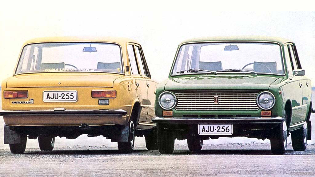 Two vintage Lada 1200 cars, one yellow and one green, parked side by side on a foggy day, with matching license plates reading auj-255 and auj-256