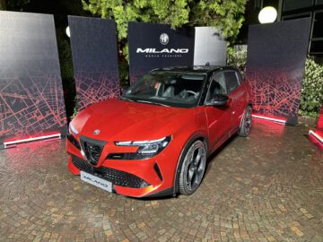 Een rode alfa romeo tonale SUV geparkeerd op een evenement, tentoongesteld voor zwarte panelen met "milano" en het merklogo.