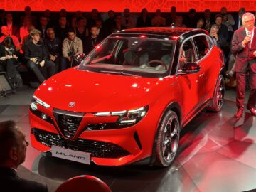 Rode Alfa Romeo Milano SUV onthulling op een autoshow met mensen in het publiek en een presentator aan de zijkant.