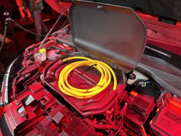 Een close-up van een open autokap, waar een levendige gele spiraalkabel en complexe motoronderdelen zichtbaar zijn, met zachte sfeerverlichting.