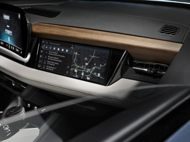 Innenraum eines modernen Autos mit einem Armaturenbrett mit großem Touchscreen-Display und einer Navigationskarte, umgeben von eleganten Holzakzenten.
