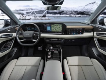Interior view of an Audi car with modern dashboard, leather seats and snow-capped mountains visible through the windshield.