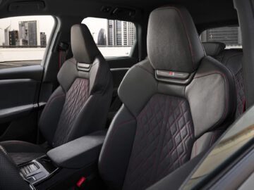 Interior view of a modern car with details of luxurious black and red stitched leather seats with the city skyline visible in the background.