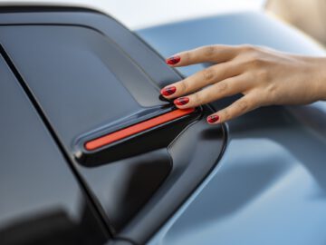 Een hand met rode nagellak rust op de achterspoiler van een Citroën C3.