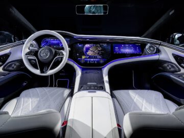 Binnenaanzicht van een Mercedes-Benz EQS met digitaal dashboard, lederen stoelen en sfeerverlichting.
