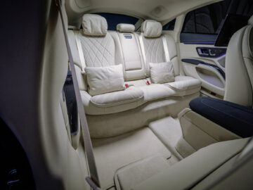 Interior de un Mercedes-Benz EQS con lujoso asiento trasero de cuero blanco con elegantes costuras, iluminación ambiental azul y moqueta limpia.