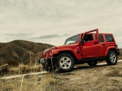 Een rode SUV met een open bestuurdersdeur staat off-road geparkeerd in een droog, heuvelachtig gebied onder een bewolkte hemel, wat lijkt op het ruige terrein dat je zou kunnen aantreffen in een spannend 'gokkasten'-thema.