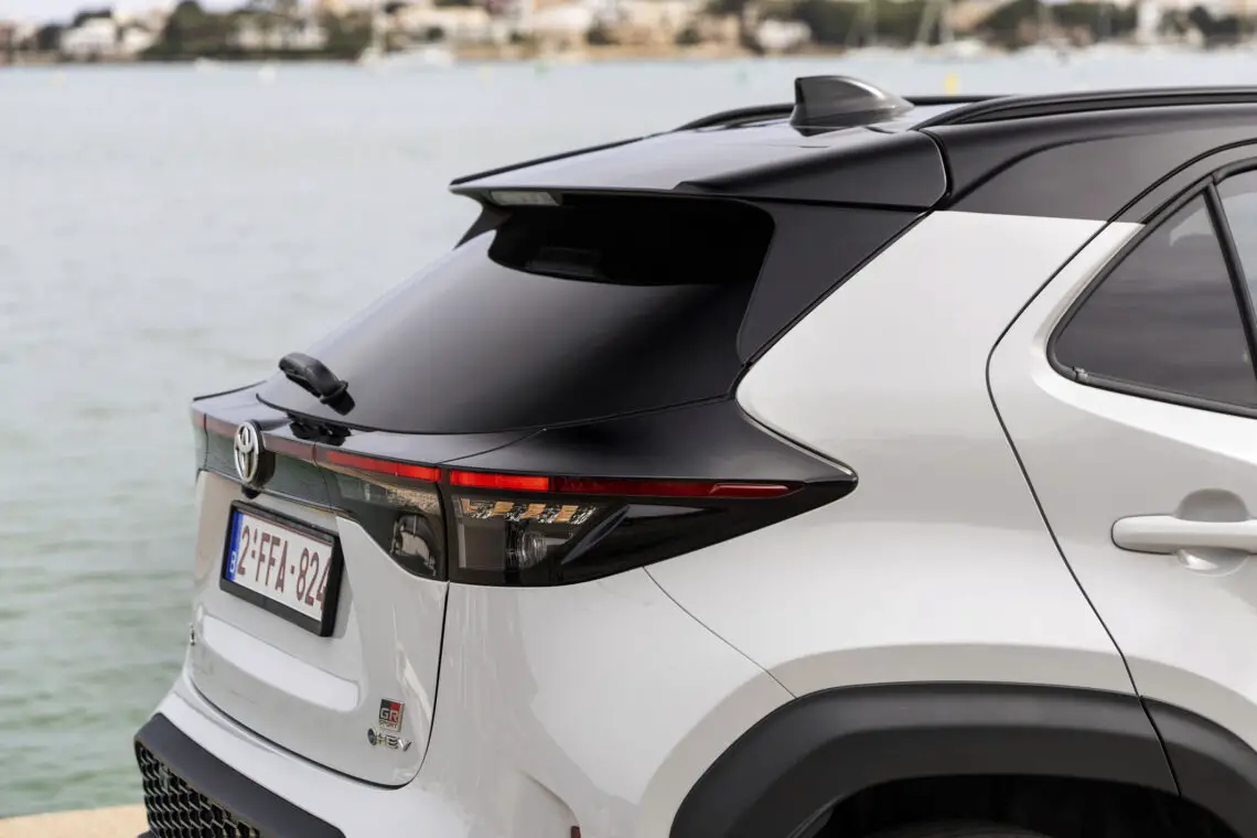 Rückansicht eines weißen Toyota Geländewagens, der am Wasser geparkt ist, wobei die Rückleuchten, die Heckscheibe und der Bereich des Nummernschilds zu sehen sind - ein Blick auf den meistverkauften Toyota Yaris Cross mit seinem schnittigen Design und den Updates für 2024.