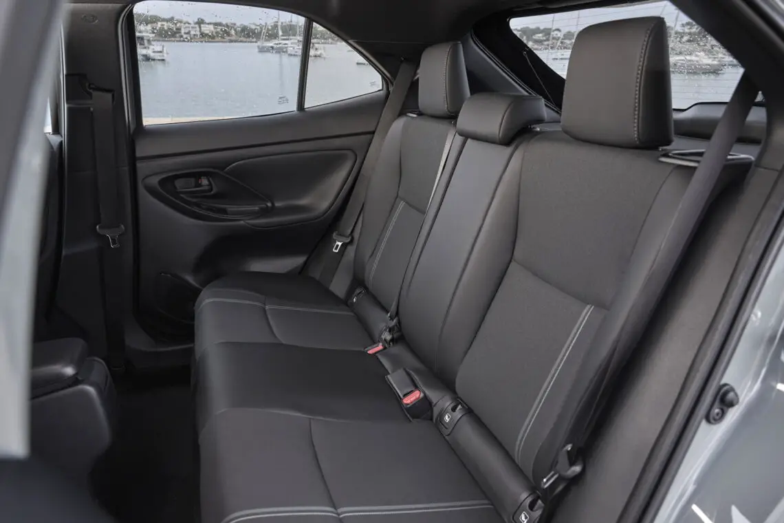 Innenansicht des Rücksitzes eines Toyota Yaris Cross aus dem Jahr 2024, mit schwarzen Ledersitzen, Sicherheitsgurten und einem Fenster mit Blick auf das Wasser und die Boote im Hintergrund.
