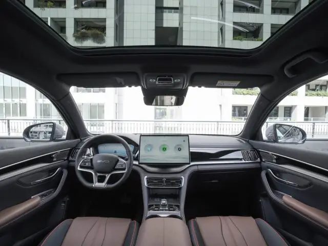 Vue de l'intérieur de la BYD SEAL U, une voiture au design moderne avec un tableau de bord numérique, un écran tactile central et un toit ouvrant panoramique.