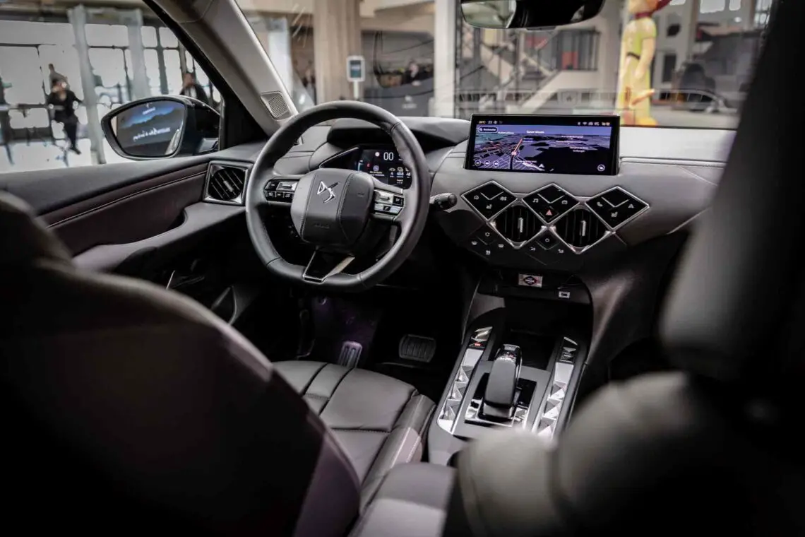 Binnenaanzicht van een moderne auto met het stuur, het digitale dashboard en het centrale display met navigatiesysteem, omringd door strakke zwartleren stoelen – een eerbetoon aan precisie en luxe die doet denken aan de exclusieve collectie van Antoine de Saint-Exupéry.