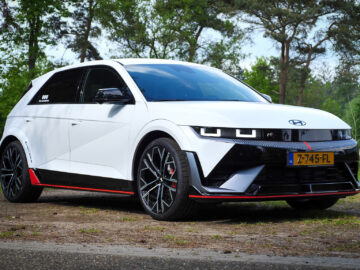 Een witte elektrische auto Hyundai Ioniq 5 N met zwarte accenten en rode details, geparkeerd op een landelijke weg omgeven door bomen en groen. Het strakke design van de Hyundai Ioniq valt op tegen de serene achtergrond van de natuur.