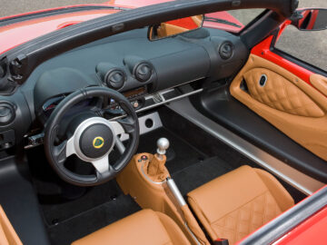Vue intérieure d'une Lotus Exige S avec des sièges en cuir marron, un levier de vitesses manuel et un tableau de bord minimaliste.