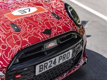 Close-up van de voorkant van een rode MINI John Cooper Works met een wit en zwart patroon, met het nummer 37 op de motorkap en een kentekenplaat met de tekst "BR24 PRO.