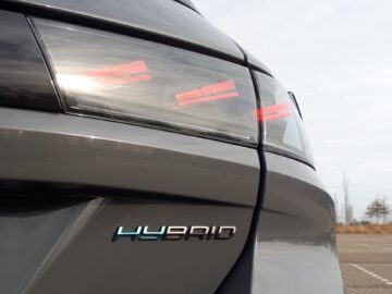 Close-up van de achterkant van een grijze Peugeot 508 SW Hybrid 225 uit 2024, met de achterlichten en een prominente 'HYBRID'-badge.