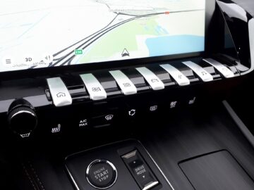 Een autodashboard met een touchscreen met daarop een kaart en verschillende knoppen voor verschillende bedieningselementen, waaronder airconditioning, stoelverwarming en rijmodi, wordt op indrukwekkende wijze tentoongesteld in de nieuwe Peugeot 2024-modellen.