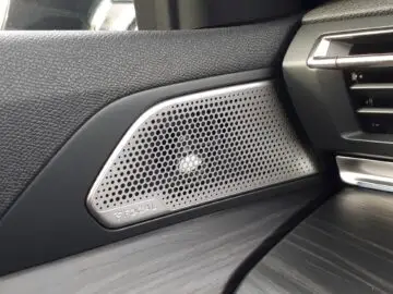 Close-up van een Peugeot 508 SW-interieur uit 2024 met een luidspreker met een geperforeerd metalen rooster, met het opschrift "FOCAL", geïntegreerd in het dashboard nabij de ventilatieopening.