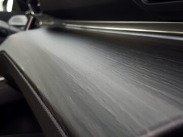 Close-up van een Peugeot 508 SW-autodashboard uit 2024 met een gladde, donkerhoutachtige afwerking met lineaire korrelpatronen.