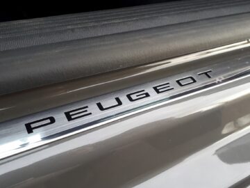 Close-up van de dorpelplaat van een Peugeot 508 SW Hybrid 225-auto met de merknaam "PEUGEOT" erop gegraveerd, wat het strakke ontwerp van het model uit 2024 laat zien.