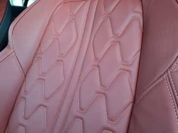 Close-up van de rugleuning van de autostoel van de Peugeot 508 SW, bekleed met roodbruin leer met ingewikkelde stikpatronen en geperforeerde zijpanelen. De Hybrid 225 uit 2024 getuigt van onberispelijke aandacht voor detail.