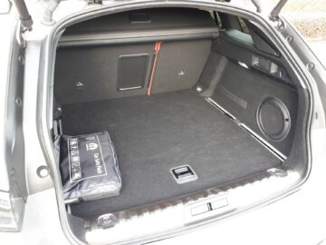 De afbeelding toont de lege kofferruimte van een Peugeot 508 Hybrid 225 met de achterdeur open. Aan de linkerkant van de met tapijt beklede kofferbak is een autogereedschapsset bevestigd.