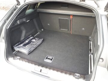 Het interieur van de kofferbak van de Peugeot 508 SW Hybrid, zoals benadrukt in de recensie van 2024, is voorzien van een zwarte tas aan de linkerkant. De kofferbak is voorzien van vloerbedekking en enkele opbergvakken aan de zijkanten.