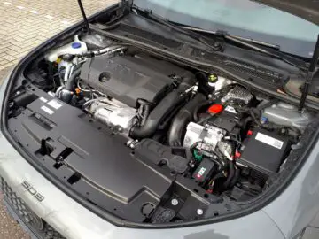 Een open autokap met daarop de motor en verschillende componenten van de motorruimte van de Peugeot 508 SW Hybrid, die een gedetailleerd beeld biedt van een uitgebreide recensie van 2024.