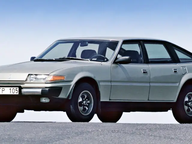 Een zilveren Rover 3500 vintage hatchback uit 1977 staat geparkeerd op een vlakke ondergrond met een helderblauwe lucht op de achtergrond. De auto, die trots zijn D-TP 105-kentekenplaat pronkt, is voorzien van zwarte details op de bumpers en wielkasten: werkelijk een lust voor het oog *gespot*.