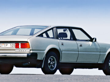 Une Rover 3500 à hayon de 1977, de couleur argentée, est garée avec une vue de l'arrière et du côté. La voiture, dotée d'un numéro d'immatriculation européen et d'une ligne de toit inclinée, est d'une élégance intemporelle dans cet instant nostalgique.