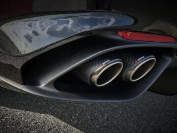 Close-up van de dubbele uitlaatpijpen van een auto met een koolstofvezelafwerking, die de lucht weerspiegelen en omgeven zijn door een glanzend verfoppervlak. Dit Alfa Romeo Quadrifoglio-model straalt een aura uit van verfijnde prestaties en Italiaans vakmanschap.