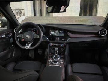 Binnenaanzicht van een moderne Alfa Romeo-auto met een met leer bekleed stuur, een digitaal dashboard, een aanraakscherm en verschillende bedieningselementen op de middenconsole. Het Quadrifoglio-embleem voegt een vleugje erfgoed en prestatieflair toe.