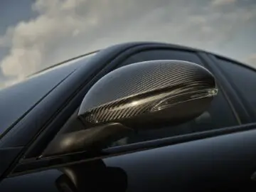 Close-up van de koolstofvezel zijspiegel van een Alfa Romeo Quadrifoglio tegen een bewolkte hemelachtergrond, die de essentie van Super Sport-techniek vastlegt.