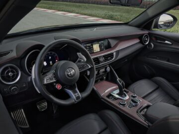 Binnenaanzicht van een Alfa Romeo Quadrifoglio met een zwart lederen stuur, een centraal touchscreen-display en lederen stoelen. Het dashboard en de middenconsole zijn voorzien van rode stiksels en koolstofvezelaccenten, waardoor het een Super Sport-esthetiek krijgt.