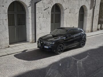 Een strakke zwarte Alfa Romeo staat geparkeerd in een geplaveide straat voor een stenen gebouw met boogramen.
