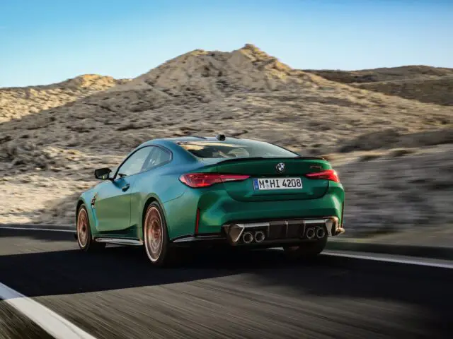 A green BMW M4 speeding on a desert highway with mountains in the background.