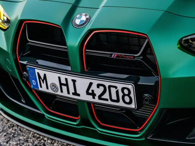 Close-up van de grille en kentekenplaat van een groene BMW M4, met opvallende rode accenten rond de ventilatieopeningen.