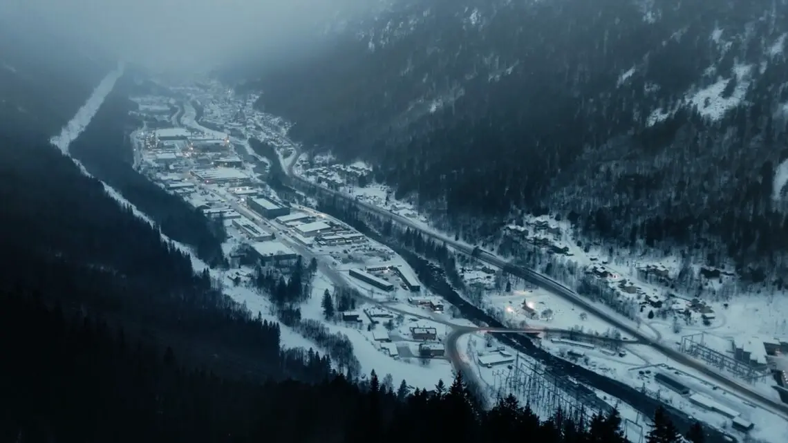 Luchtfoto van een besneeuwde vallei met een klein stadje gelegen tussen de bergen. Gebouwen, wegen en bomen zijn zichtbaar in de mistige atmosfeer en het met sneeuw bedekte landschap, waar een Hyundai IONIQ 5 N zich een weg baant door het serene wintertafereel.