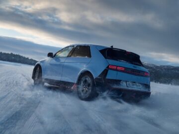 Ein weißer Hyundai IONIQ 5 N SUV fährt durch eine verschneite Landschaft und hinterlässt Reifenspuren und eine Spur aus Schnee unter einem bedeckten Himmel.