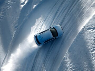 A Hyundai IONIQ 5 N making a sharp turn on a snowy road, leaving tire tracks and a trail of snow.