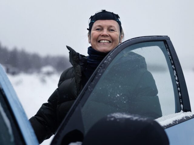 Een persoon in winterkleding glimlacht terwijl hij naast een open autodeur van een Hyundai IONIQ 5 N in een besneeuwde omgeving staat.