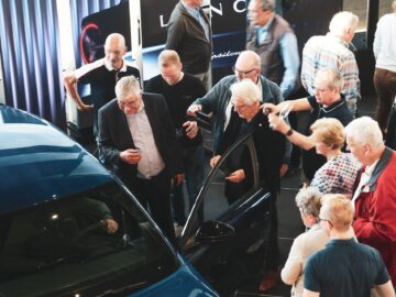 Group of people of different ages examining new Lancia cars at a show event in the Netherlands.
